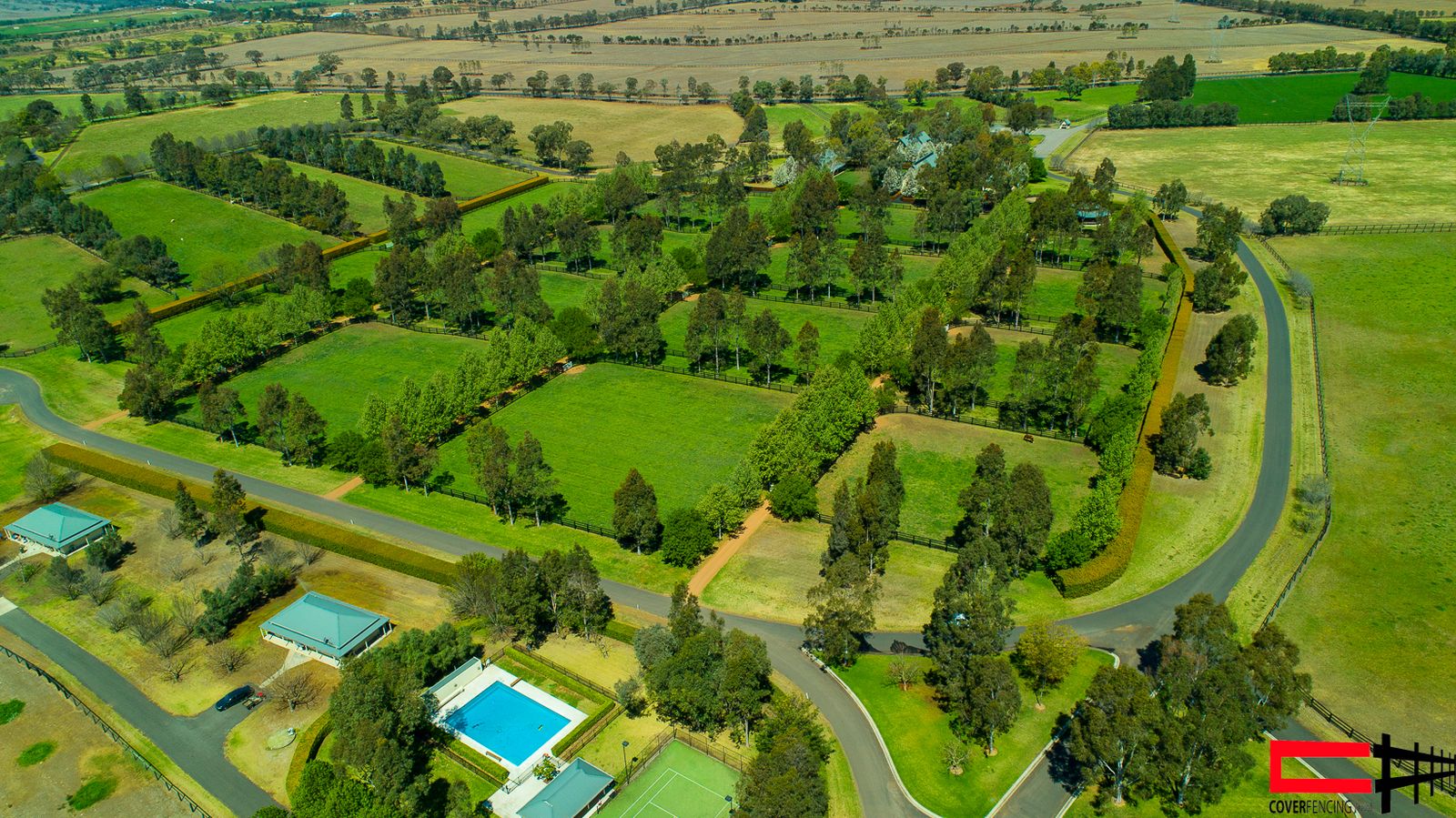 Wide aerial view of a rural property with post-and-rail fencing, pool and outbuildings